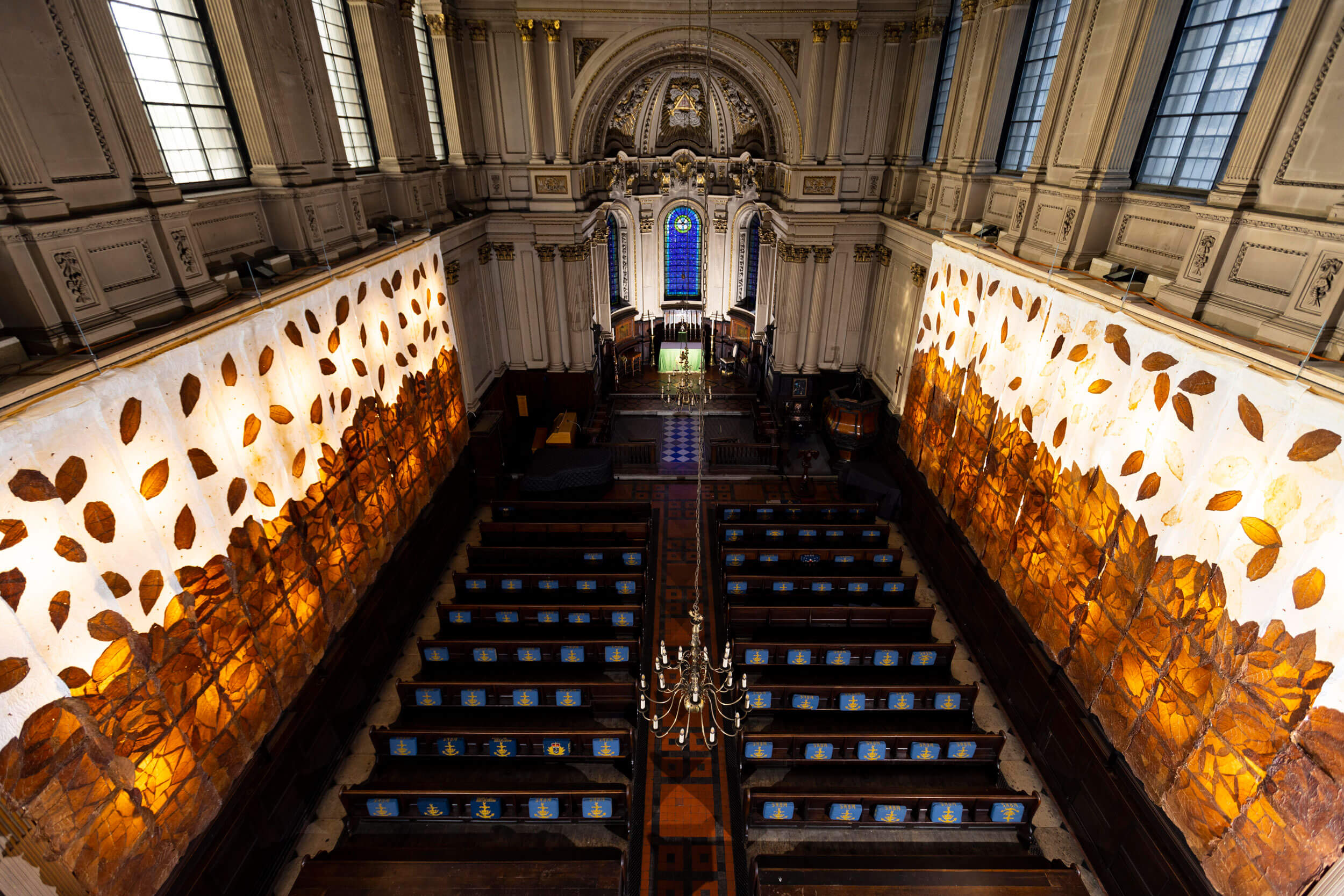 Interior de la iglesia St. Mary Le Strand en Londres, con una instalación artística moderna de hojas en paneles iluminados, contrastando con la arquitectura gótica del edificio